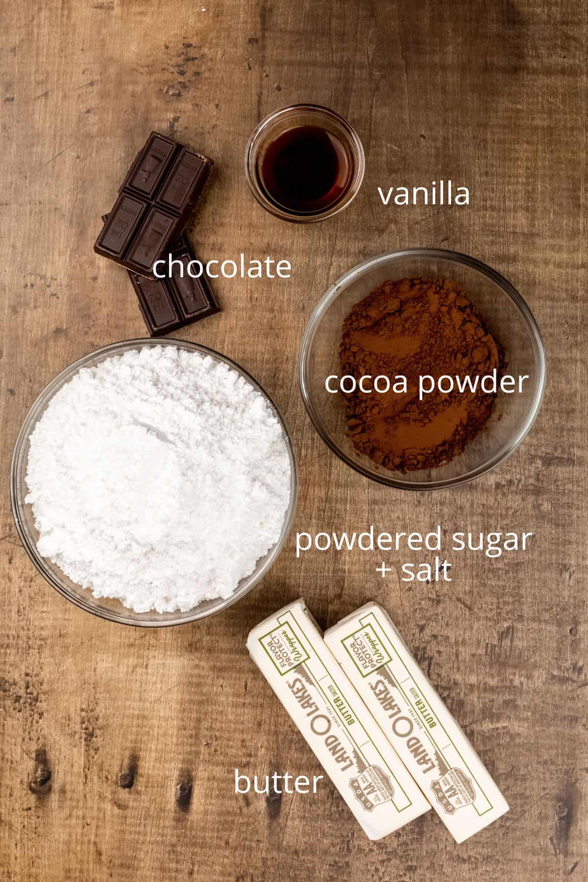 ingredients for chocolate frosting in various glass bowls on the wood kitchen table
