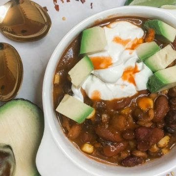 close up of black bean chocolate chili in a white bowl with avocado sour cream and hot sauce on top // livingbeyondallergies.com