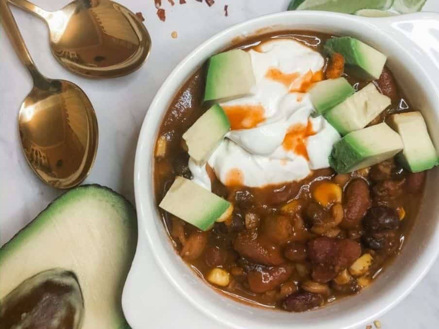 close up of black bean chocolate chili in a white bowl with avocado sour cream and hot sauce on top // livingbeyondallergies.com