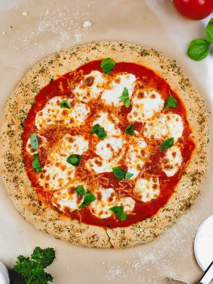 a round gluten free pizza crust brown parchment paper surrounded by tomatoes and basil and cheese