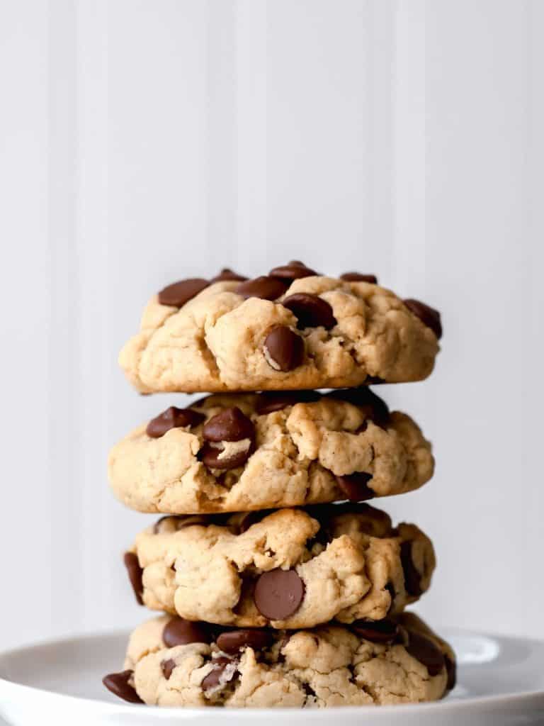 a stack of 4 gluten free vegan chocolate chip cookies are shown from the side as they are stacked on a white circle plate in front of a white background