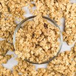 up close image of granola in a glass bowl on a baking sheet surrounded by granola