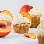 peach cobbler cupcakes are shown on the kitchen countertop surrounded by cut open peaches and peach slices