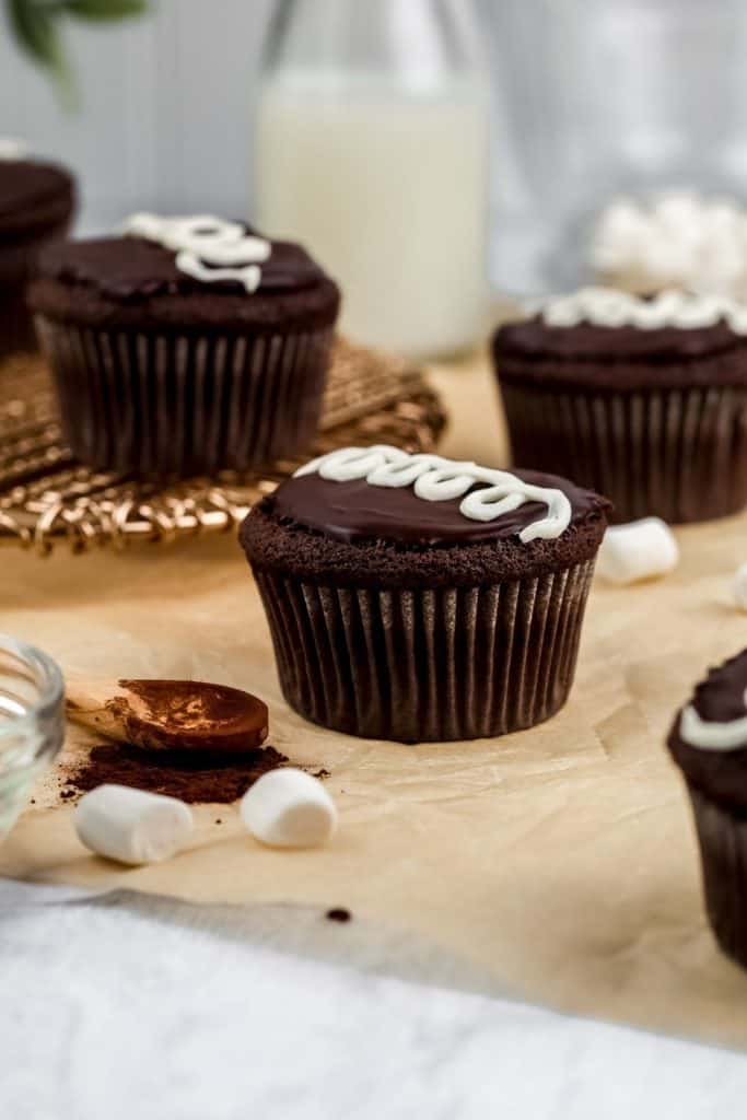 an up close image of copycat hostess cupcakes with cocoa powder, marshmallows, and other cupcakes surrounding it as it rests on the kitchen countertop