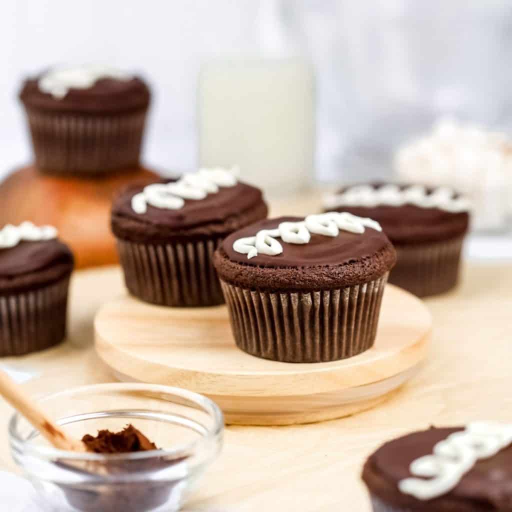 gluten free and vegan hostess cupcakes copycat recipe are seen on the countertop on various wooden platforms surrounded by ingredients like chocolate and milk