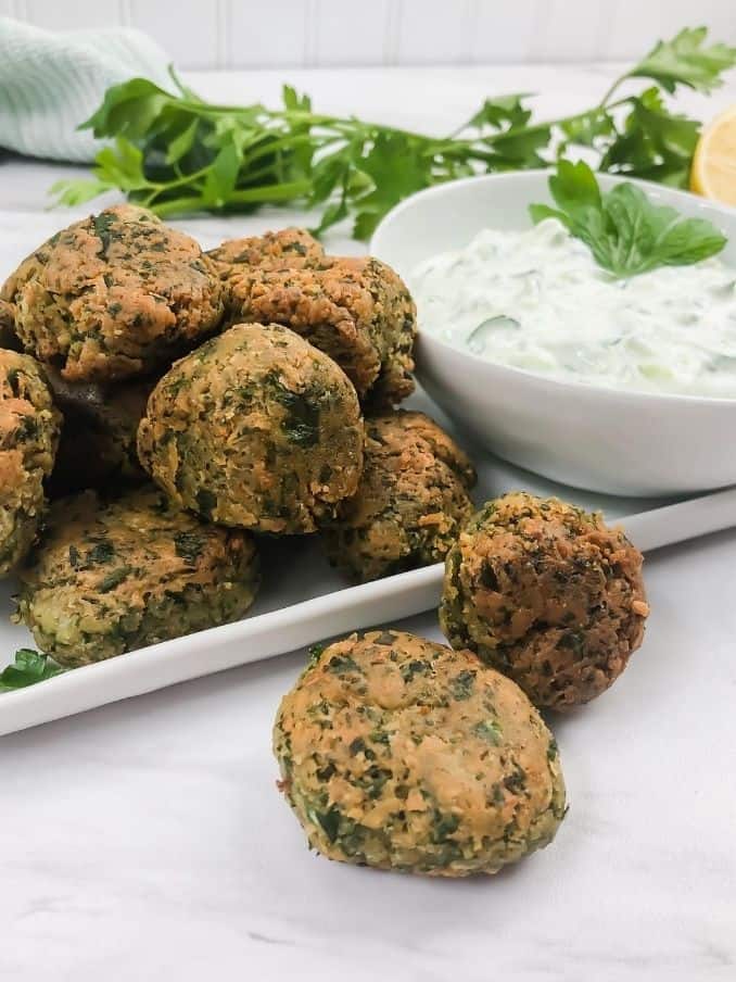 vegan gluten free falafel on a plate with yogurt dipping sauce on a white marble table with fresh parsley surrounding // livingbeyondallergies.com