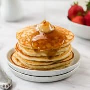 easy gluten free vegan pancakes in a stack on a white plate on a white table with strawberries and syrup // livingbeyondallergies.com