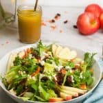 apple cider dressing next to a salad bowl filled with salad and apple slices on white table with decorations // livingbeyondallergies.com