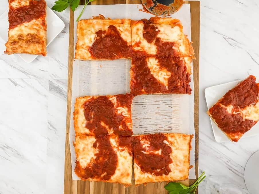 slices of detroit style gluten free pizza crust on a white countertop with the pizza in the middle