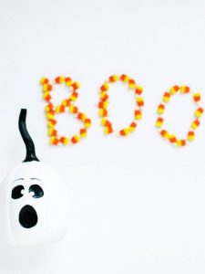 white pumpkin with a ghost painted onto the face and candy corn that spells out boo
