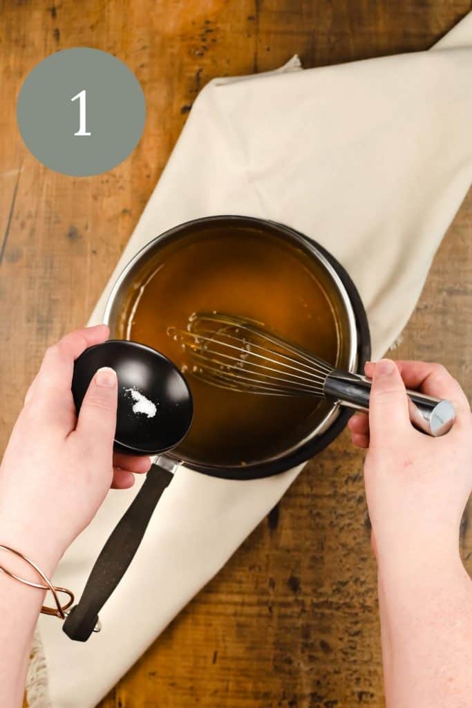 a pair of caucasian hands are shown adding salt to a silver pot of caramel sauce