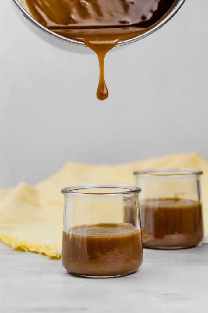 pouring caramel into glass jars with a big drip falling in the photo