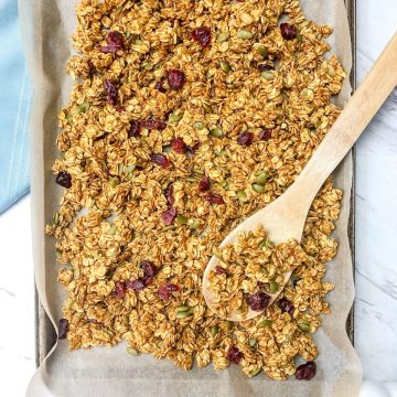 pumpkin granola on a baking tray with a wood spoon