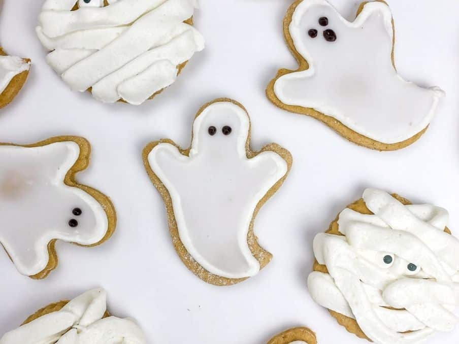 close up of pumpkin sugar cookies cut out in ghosts and mummies on a white table