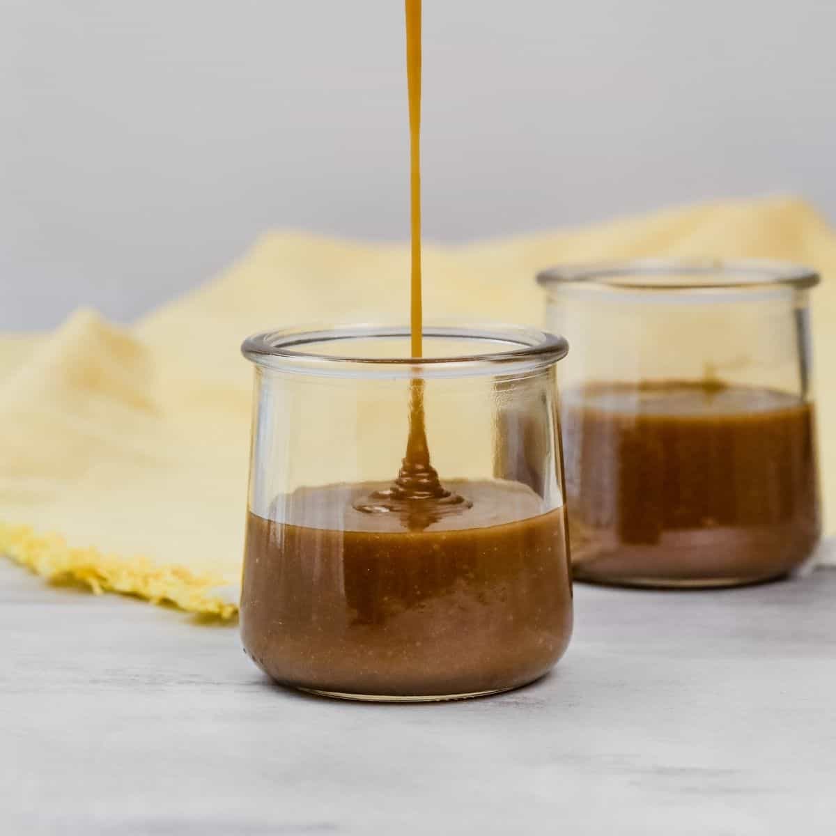 easy dairy free caramel sauce being poured into a small glass jar with a yellow towel behind it
