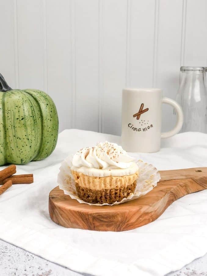 no bake mini pumpkin cheesecake on a wood cutting board with a green pumpkin and ingredients surrounding it on the countertop