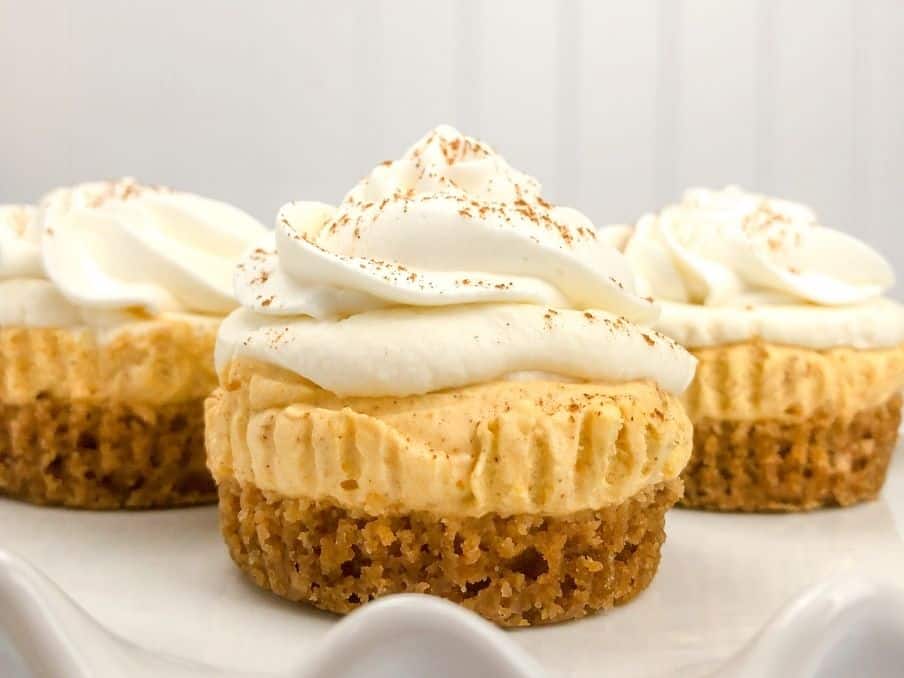 three no bake mini pumpkin cheesecakes on a white cupcake stand on the countertop