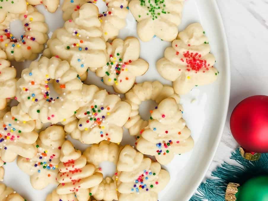 close up of gluten free spritz cookies with sprinkles on a white plate