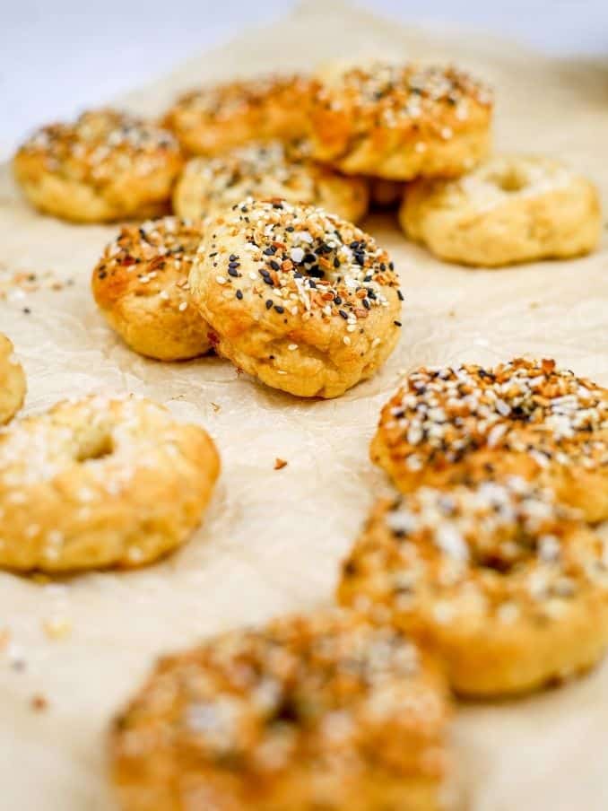a table is covered in white parchment paper with mini gluten free and vegan bagels artfully scattered around the table. everything bagel seasoning is shown scattered on the paper. // livingbeyondallergies.com