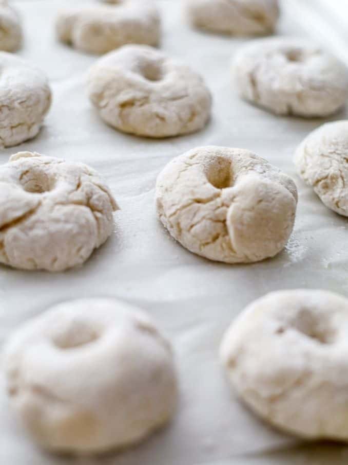 close up of mini gluten free vegan bagels after they have proofed for one hour. they rest on a white parchment sheet on a baking tray // livingbeyondallergies.com