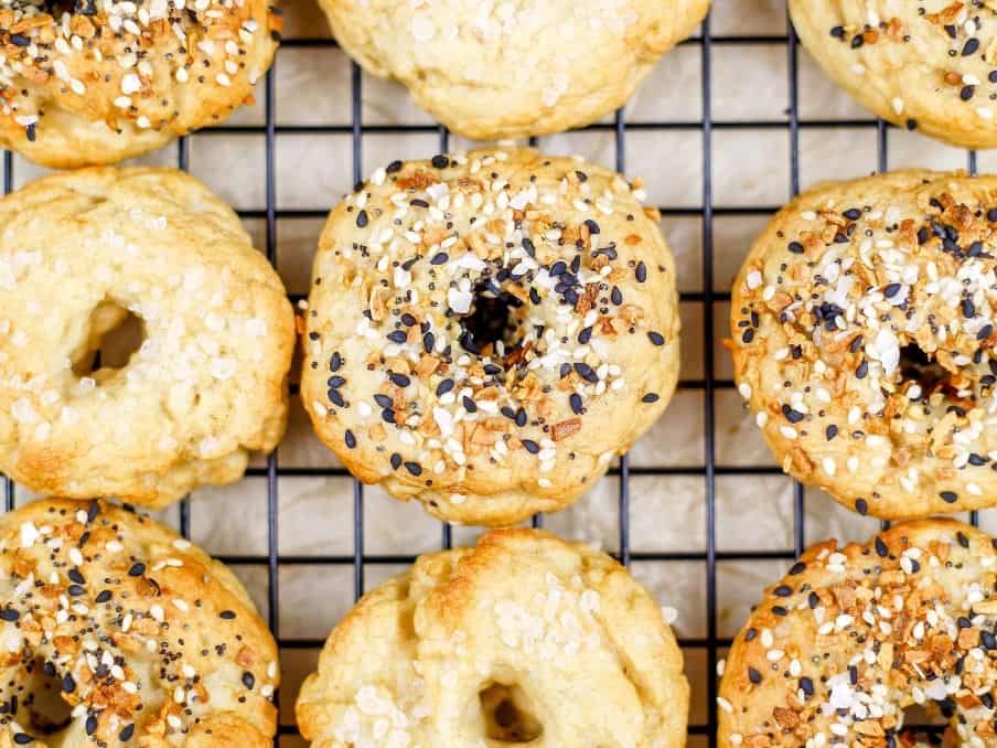 close up of gluten free vegan bagels on a black cooling rack and white parchment paper. the bagels are covered in coarse sea salt or everything spices // livingbeyondallergies.com