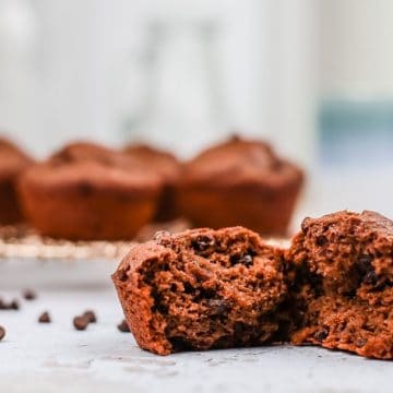 close up of gluten free vegan double chocolate muffins with one muffin in the foreground opened so you can see the delicious texture inside with more muffins in the background