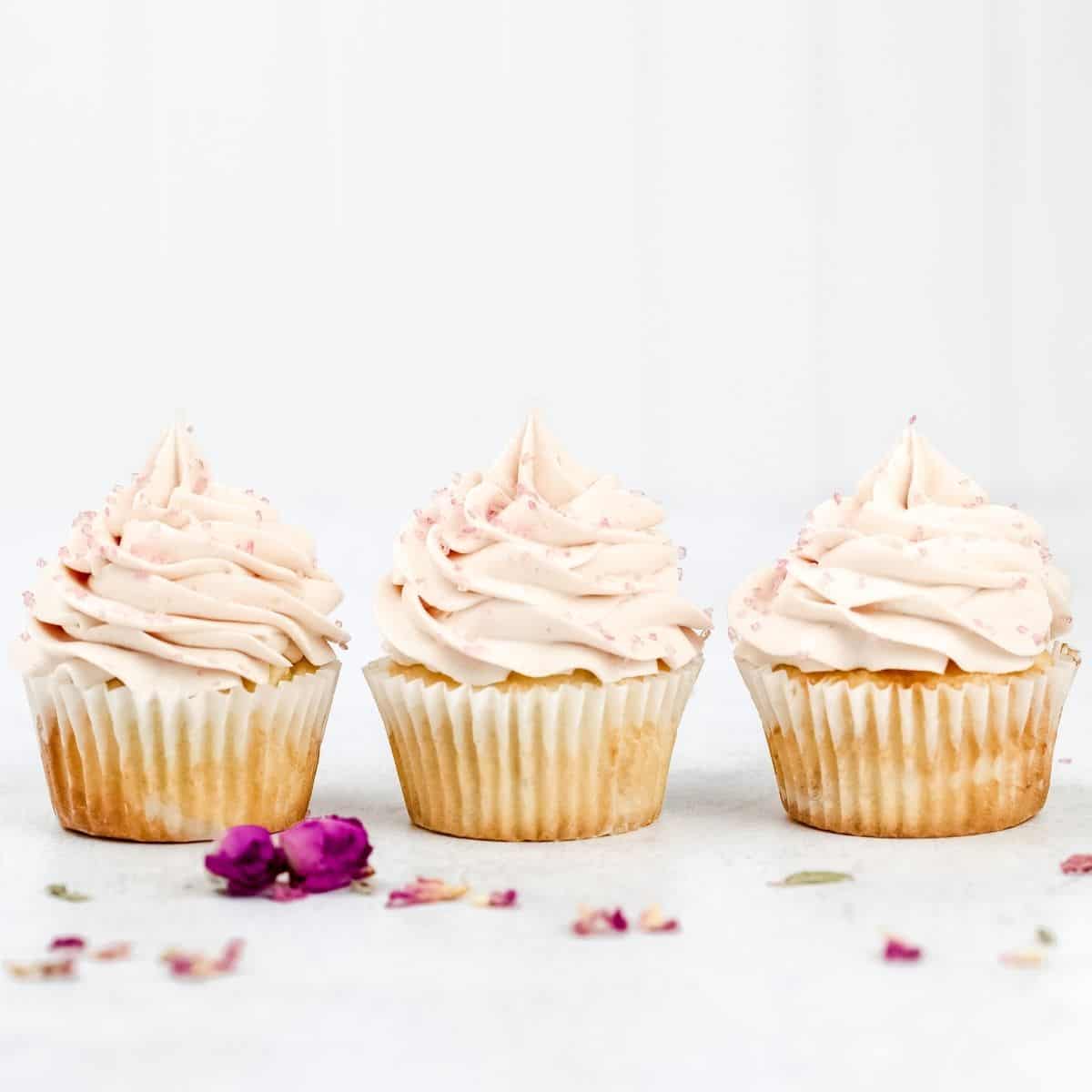 three vanilla cupcakes with rosewater buttercream frosting in a row