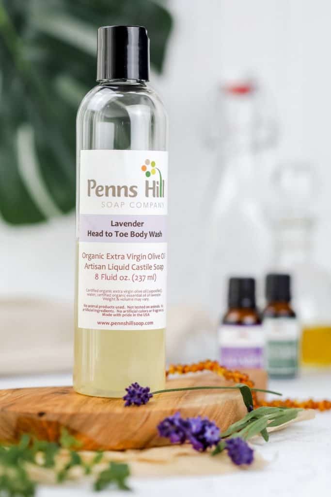 a close up of the penns hill soap company liquid Castile soap bottle on the kitchen countertop surrounded by fresh herbs and essential oils