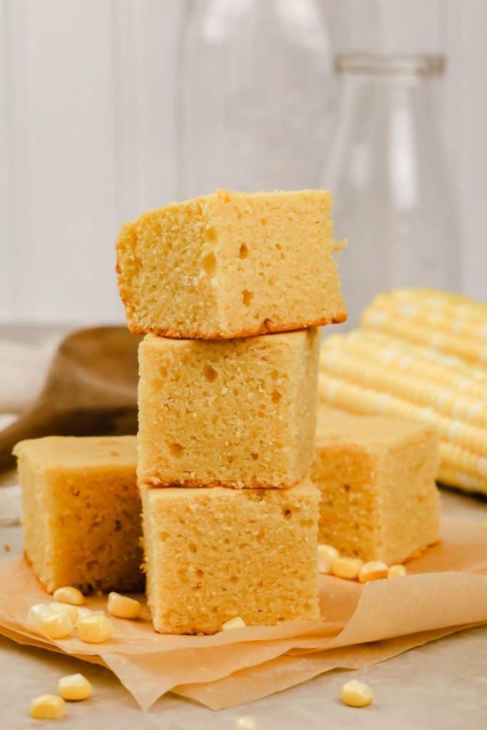 a stack of gluten free cornbread on the countertop surrounded by ears of corn and corn kernels 