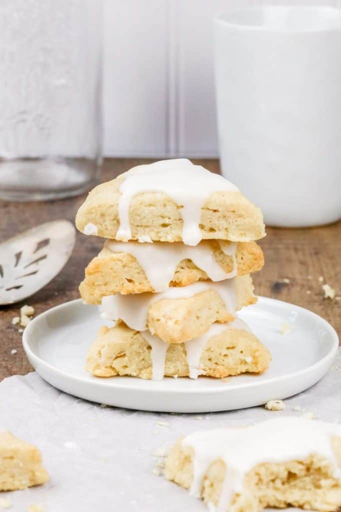 a stack of 4 vanilla scones on a round white plate with more scones and other kitchen tools surrounding them