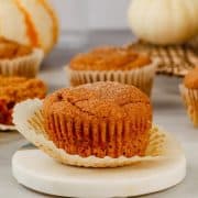 a single gluten free and vegan pumpkin muffin rests on a coaster with more muffins behind it