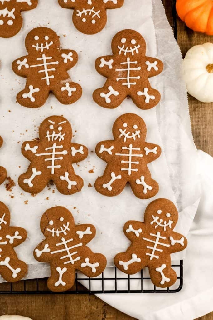many chocolate skeleton cookies on a cooling rack with mini pumpkins beside them