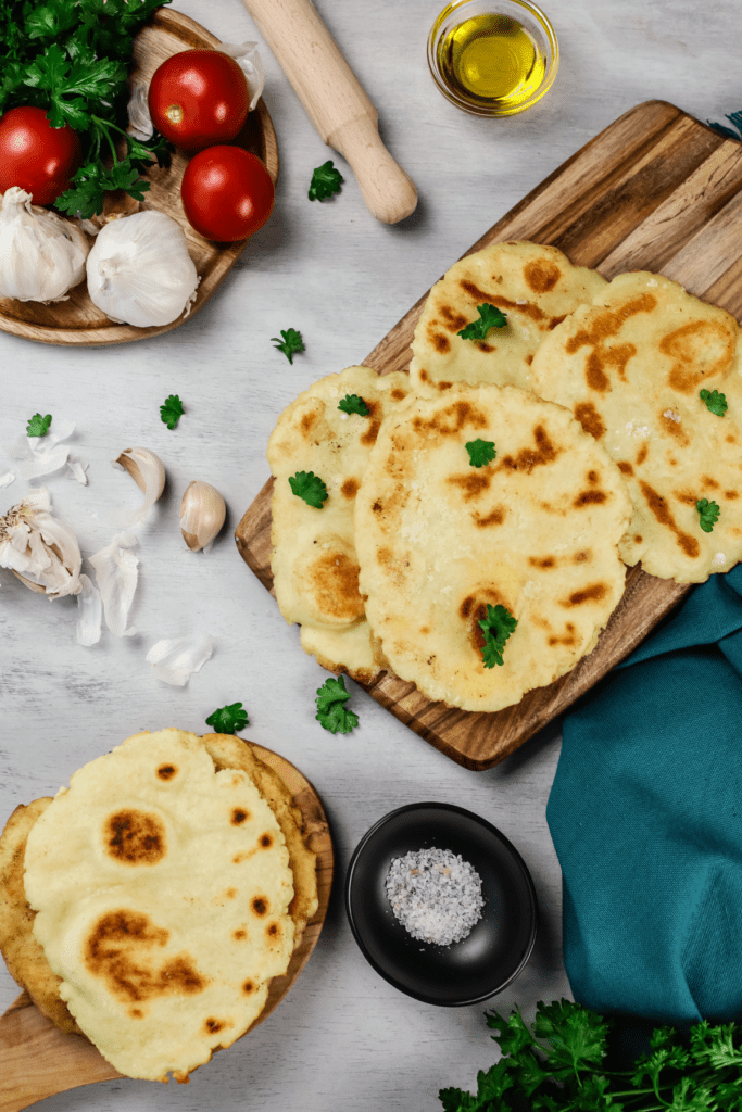 overhead view of several naan on various wood platters surrounded by ingredients 