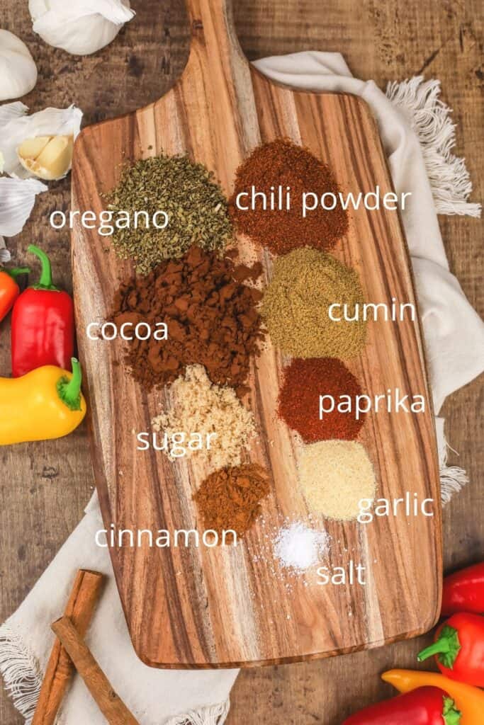 ingredients for chili seasoning on a wood cutting board surrounded by peppers
