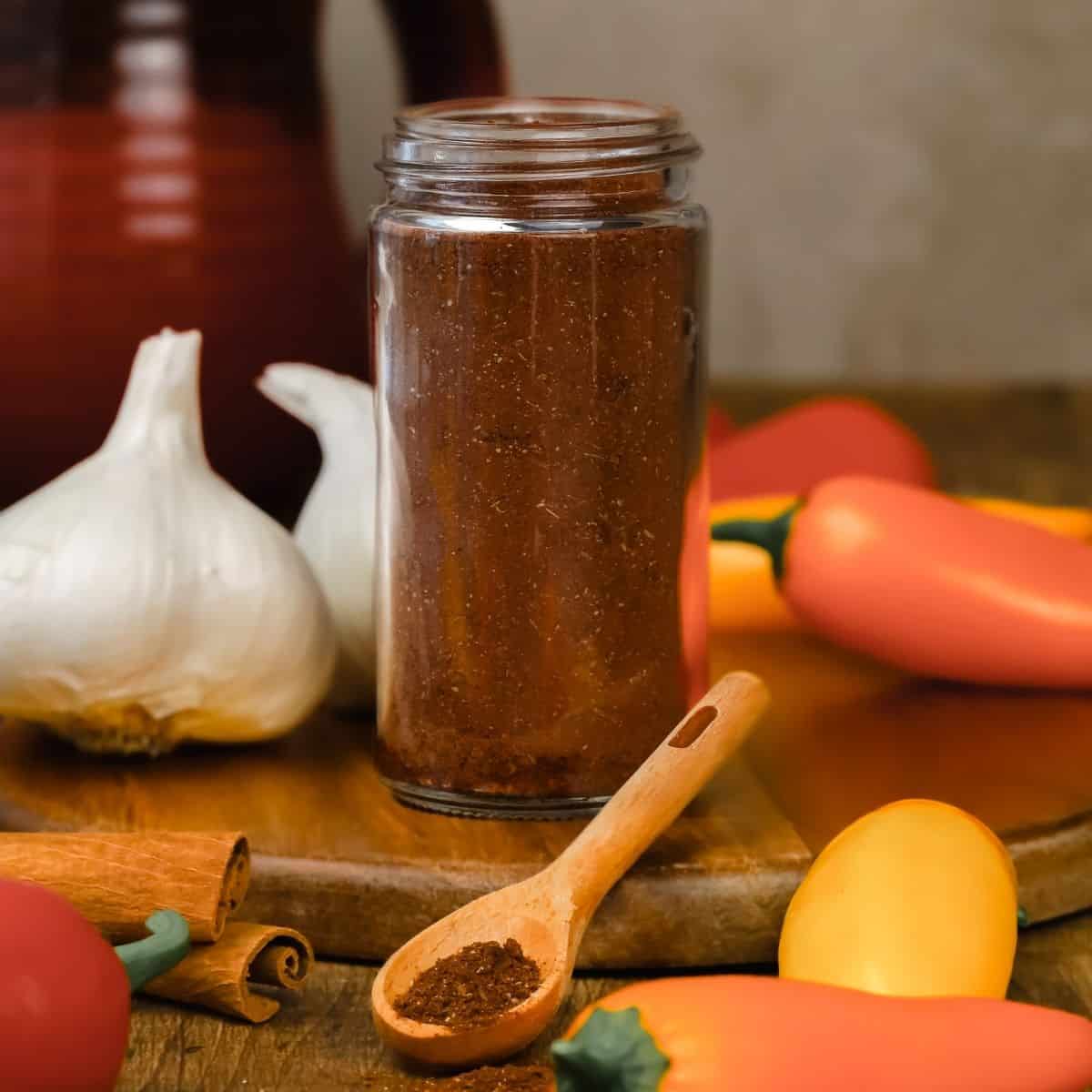 glass jar filled with homemade chili seasoning mix on the countertop next to peppers