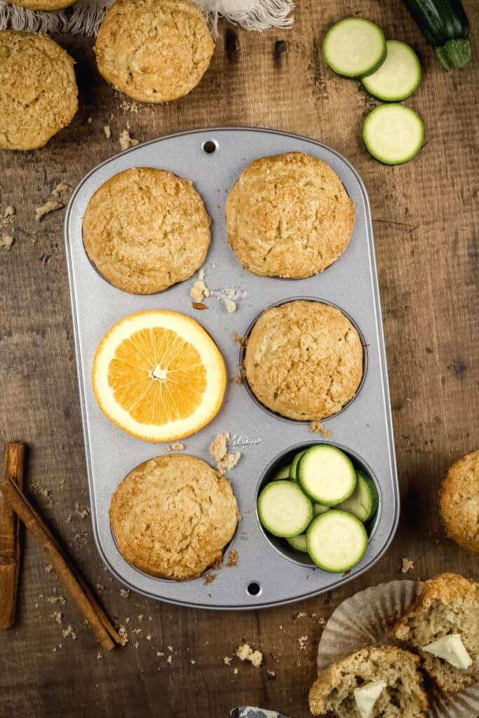gluten free zucchini muffins in a pan surrounded by ingredients and other muffins