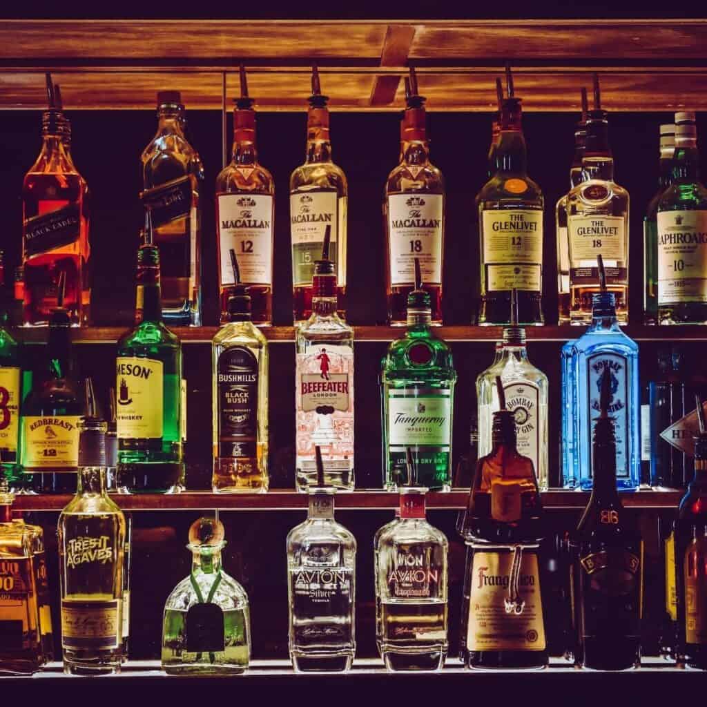 shelves filled with various alcohol bottles are backlit on a dark background