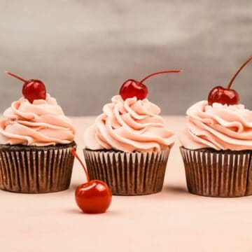 three chocolate cupcakes in a row with cherry frosting and a cherry on top of each cupcake