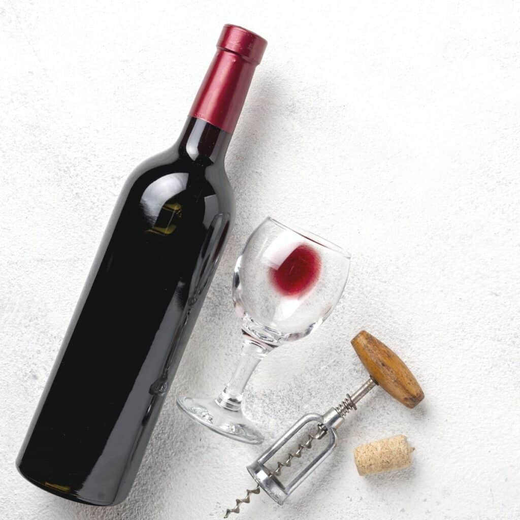 wine bottle with a glass and opener on a white surface