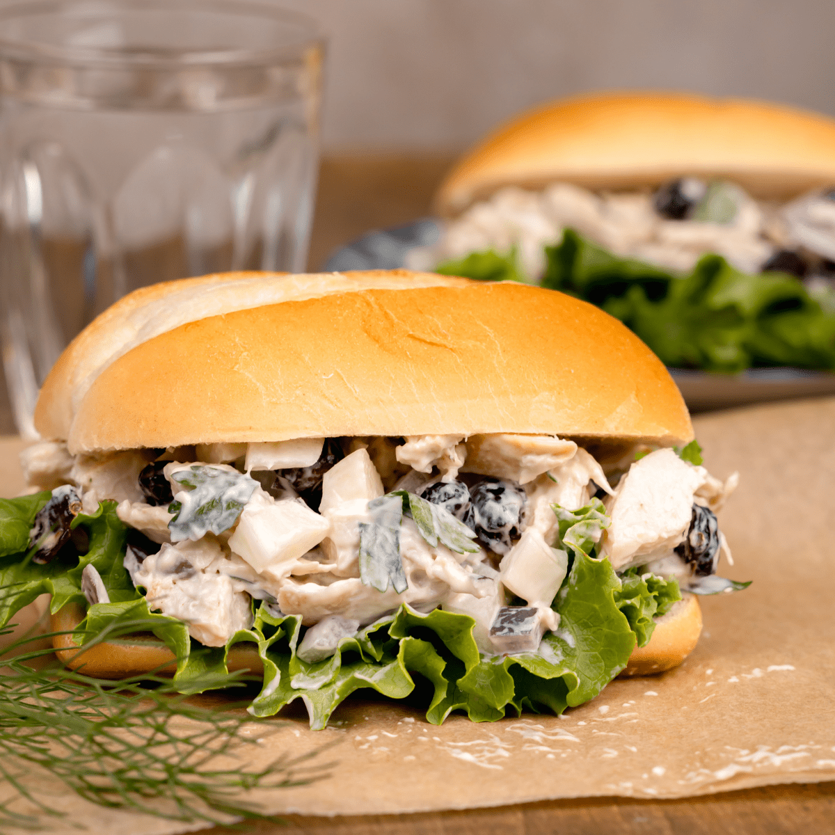 two chicken salad sandwiches with lettuce on brown parchment paper