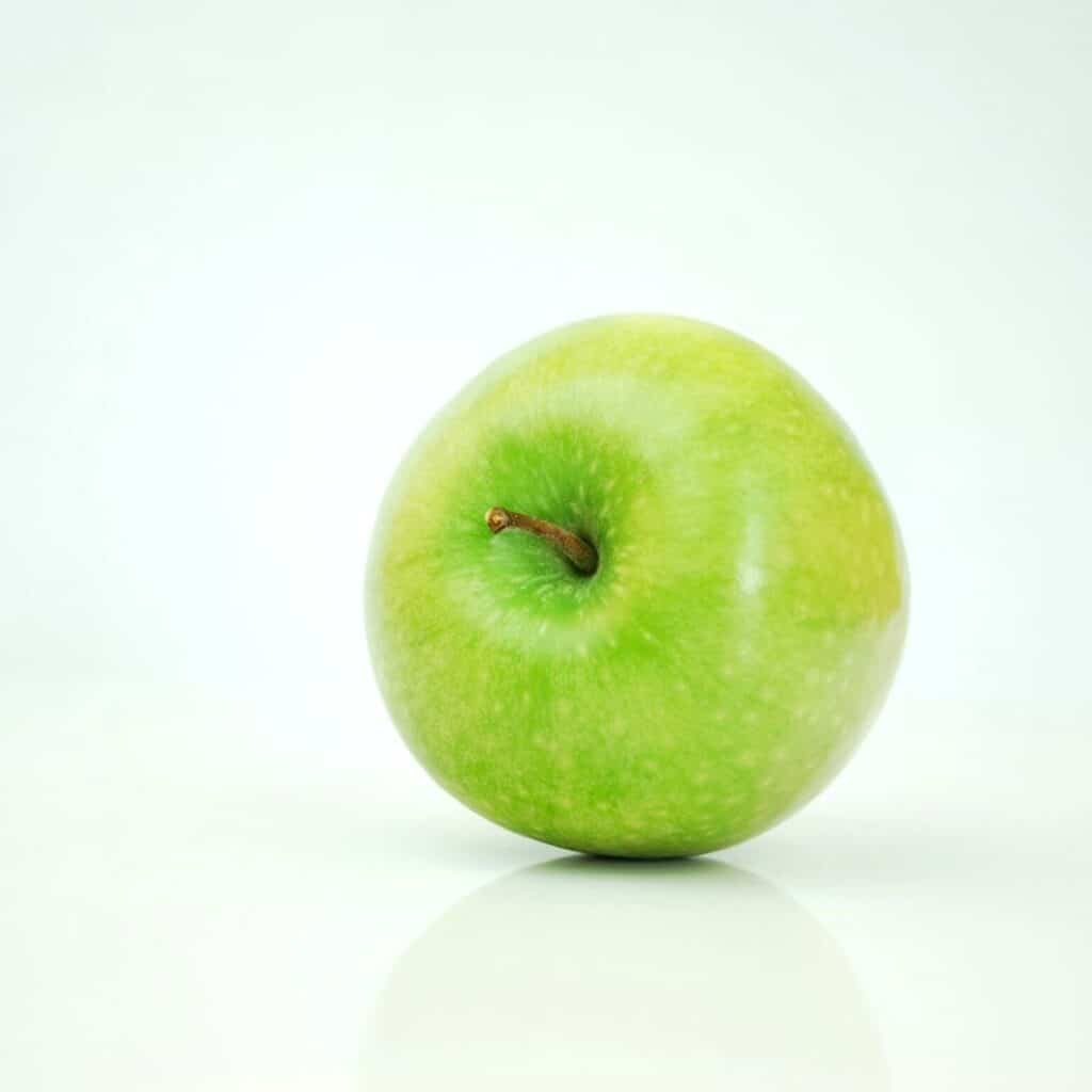 a green apple on its side on a white reflective surface