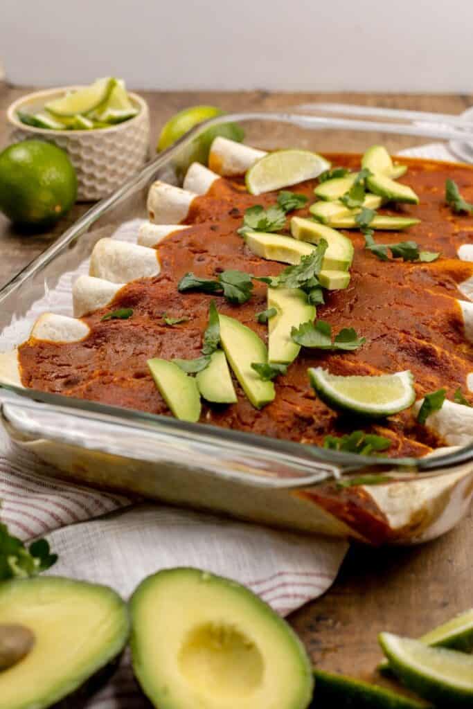 finished vegan enchiladas in a pan with avocado and lime slices on top