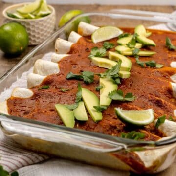 finished vegan enchiladas in a glass pan with avocado and lime slices on top