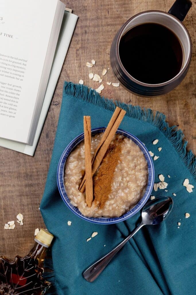 brown sugar cinnamon oatmeal in a bowl on the kitchen table with a cup of coffee and a book
