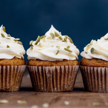 three carrot cake cupcakes without nuts in a row with swirls of frosting and crushed pumpkin seeds