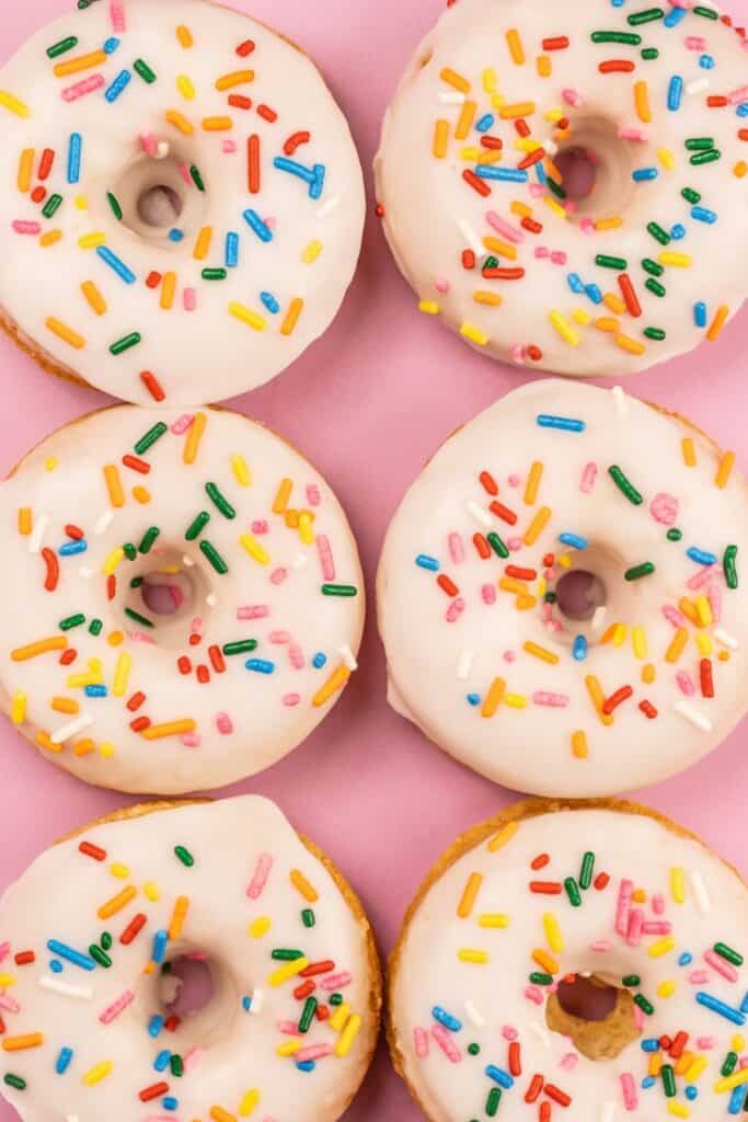 overhead view of egg free donuts with sprinkles on a pink surface
