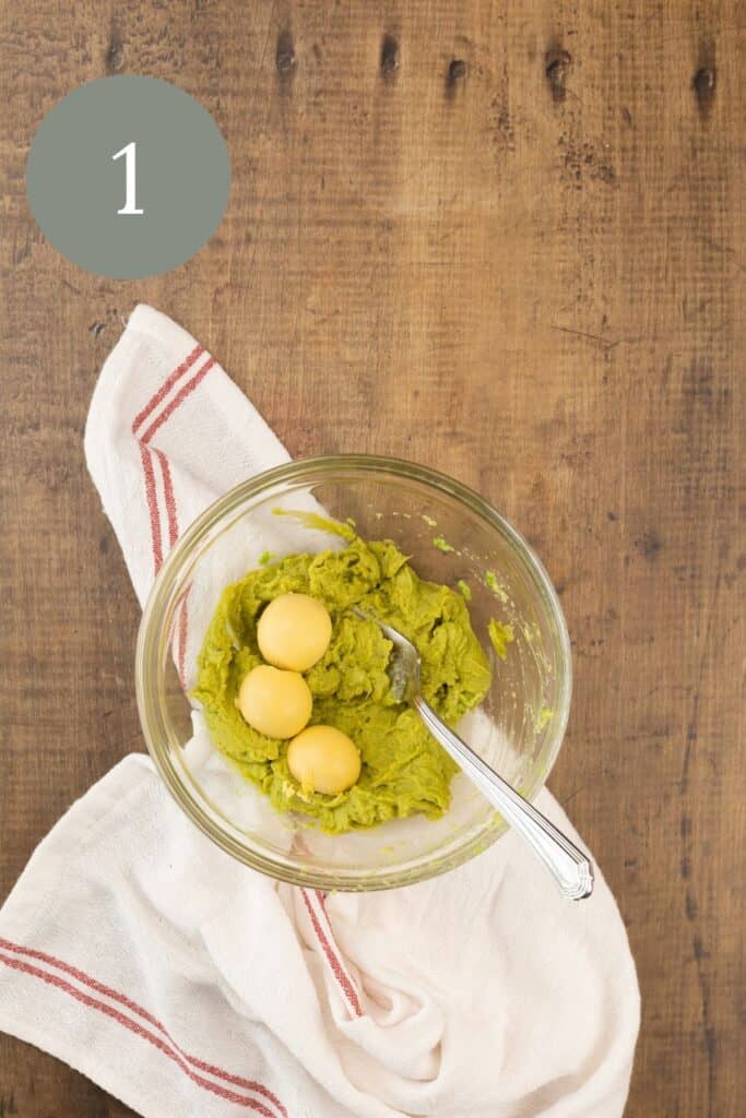 mixing the avocado and egg yolks in a glass bowl on the kitchen table