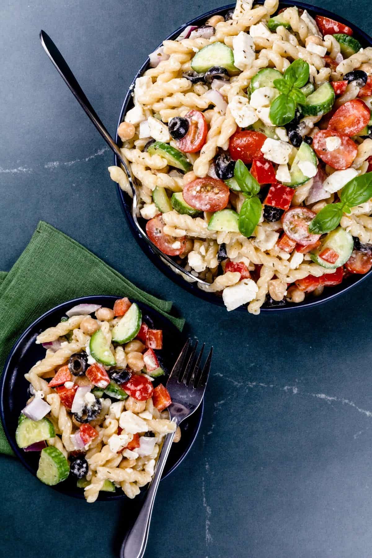 two bowls of greek pasta salad on a dark marble countertop