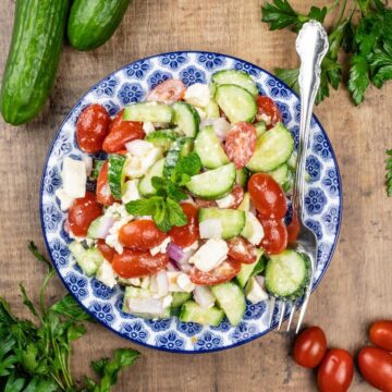 cucumber salad in a blue and white bowl with ingredients surrounding it and a fork in the bowl