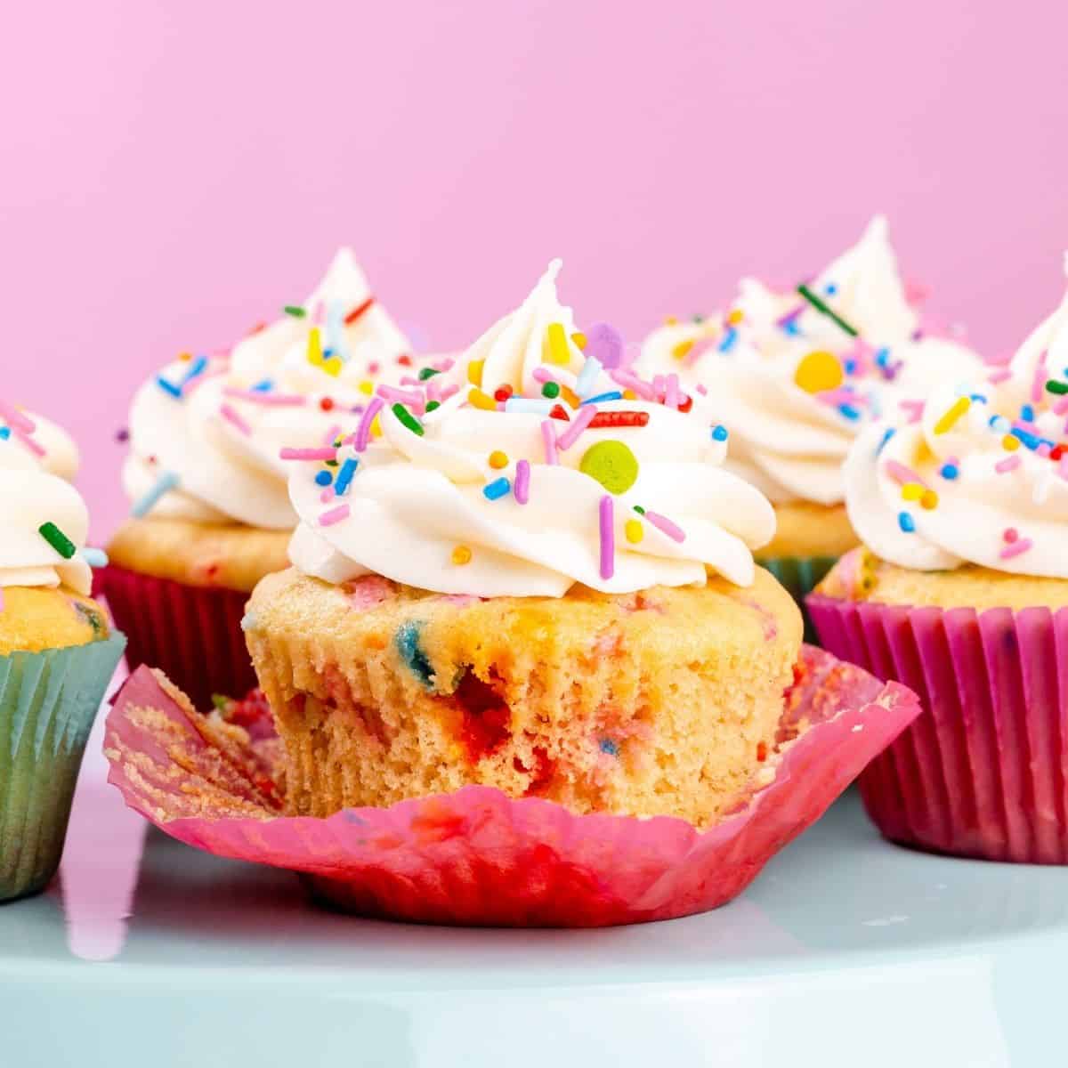 unwrapped gluten free birthday cupcakes on a stand in front of a pink background